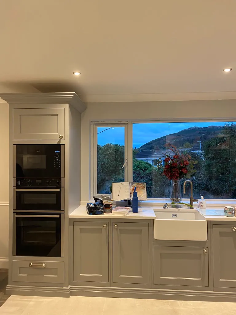 Grey painted in-frame kitchen cabinets with brass pulls and a window view