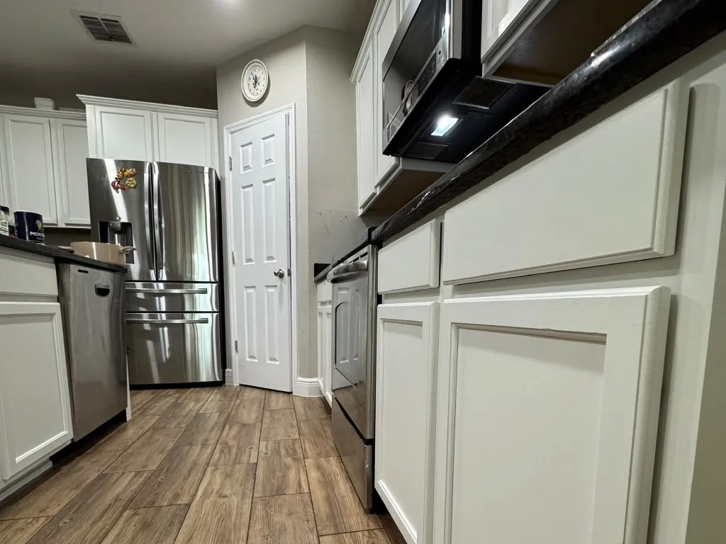 White painted kitchen cabinets and a stainless fridge down a long galley run