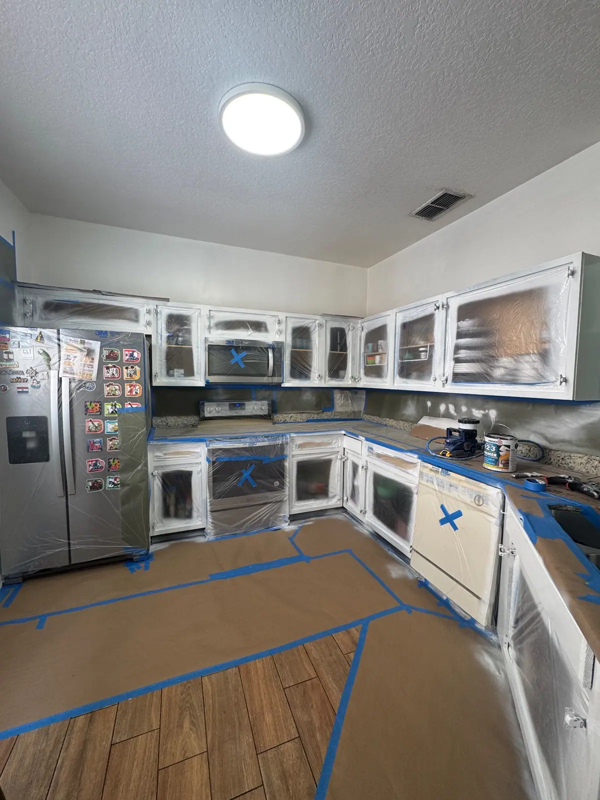 Kitchen with cabinet doors off, every opening sealed in plastic and the appliances wrapped